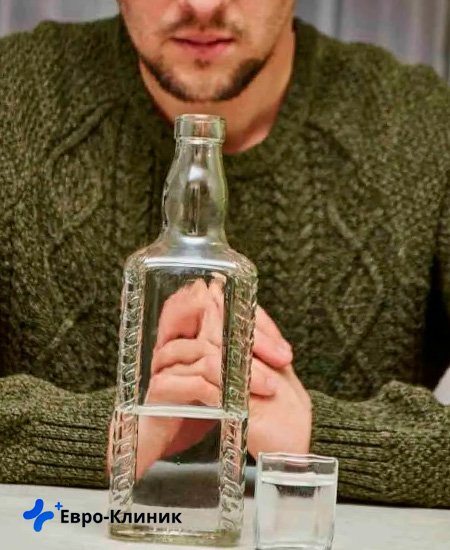 мужчина сидит за столом с бутылкой мужчина в свитере смотри на бутылку