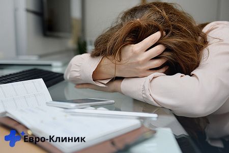 Женщина держась за голову лежит на столе